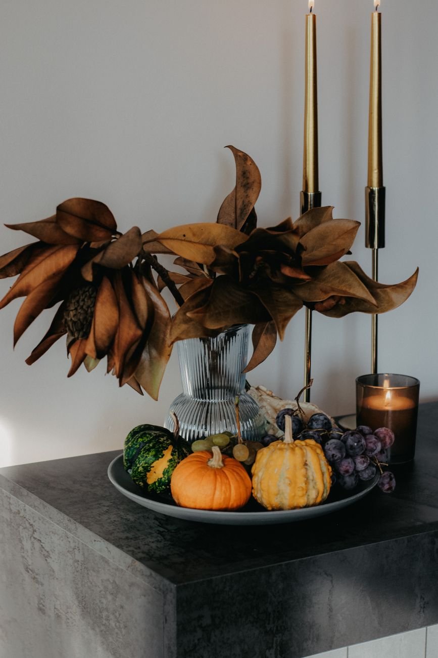 Autumn décor with small pumpkins, grapes, and dried leaves styled indoors.