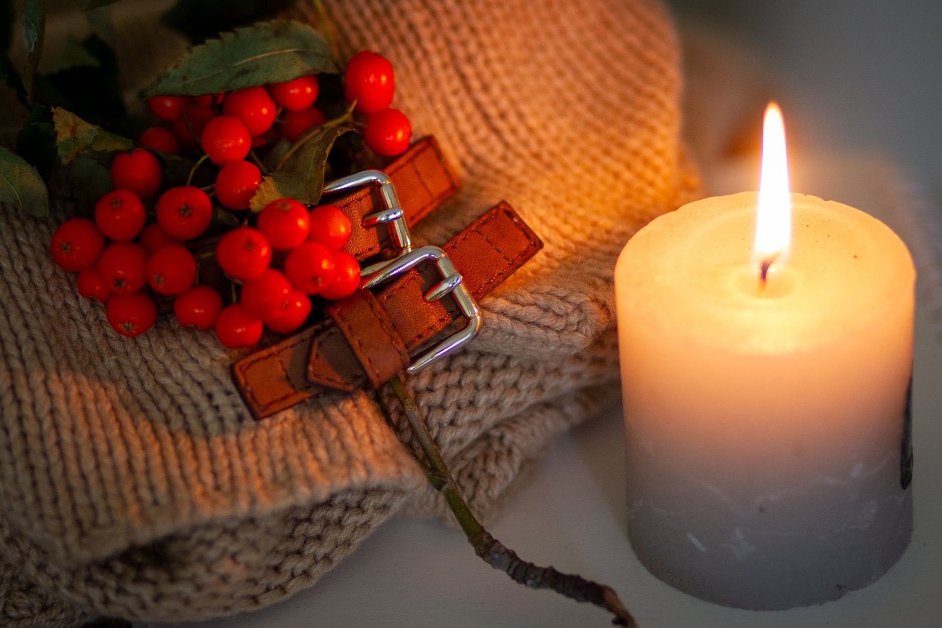 Warm candlelight with rowan berries and knit texture creates a cozy autumn atmosphere.